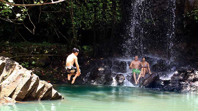 Boy jumping into water, parents sitting under waterfall watching
