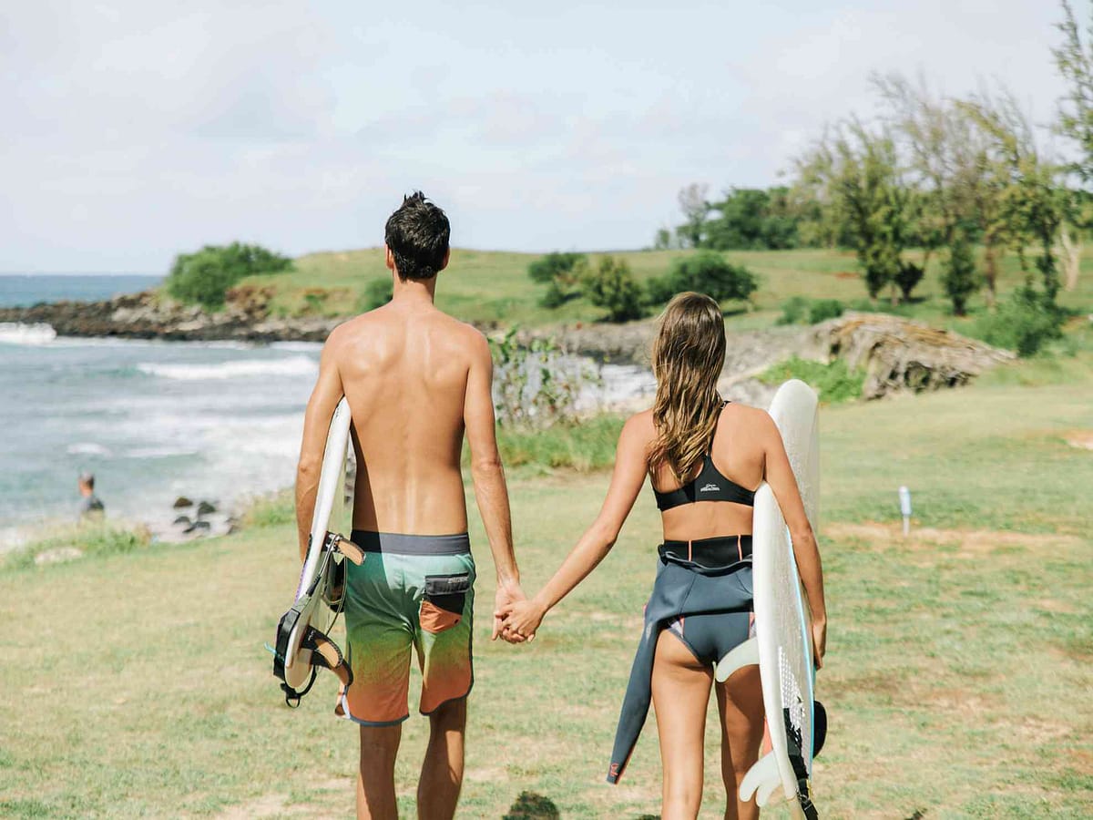 A couple walking on Molokai with two surfboards