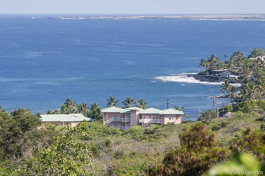 Beach villas at kahaluu with ocean and waves in background surrounded by palm trees.