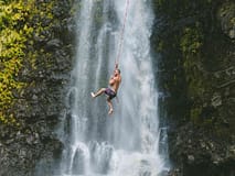 Man hanging onto rope swing at Waimea falls. One of the things to do on the big island.
