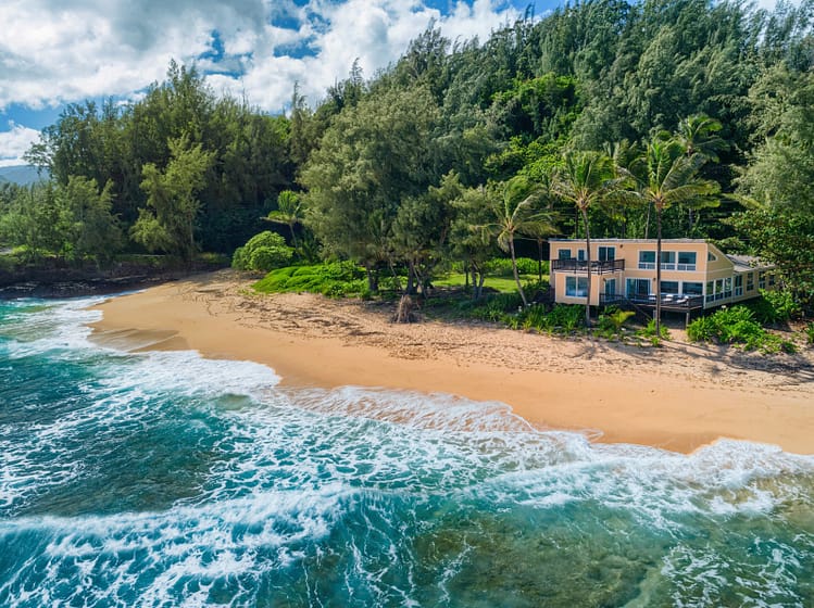 Home right on the white sand beach with waves crashing in an trees surrounding the home.